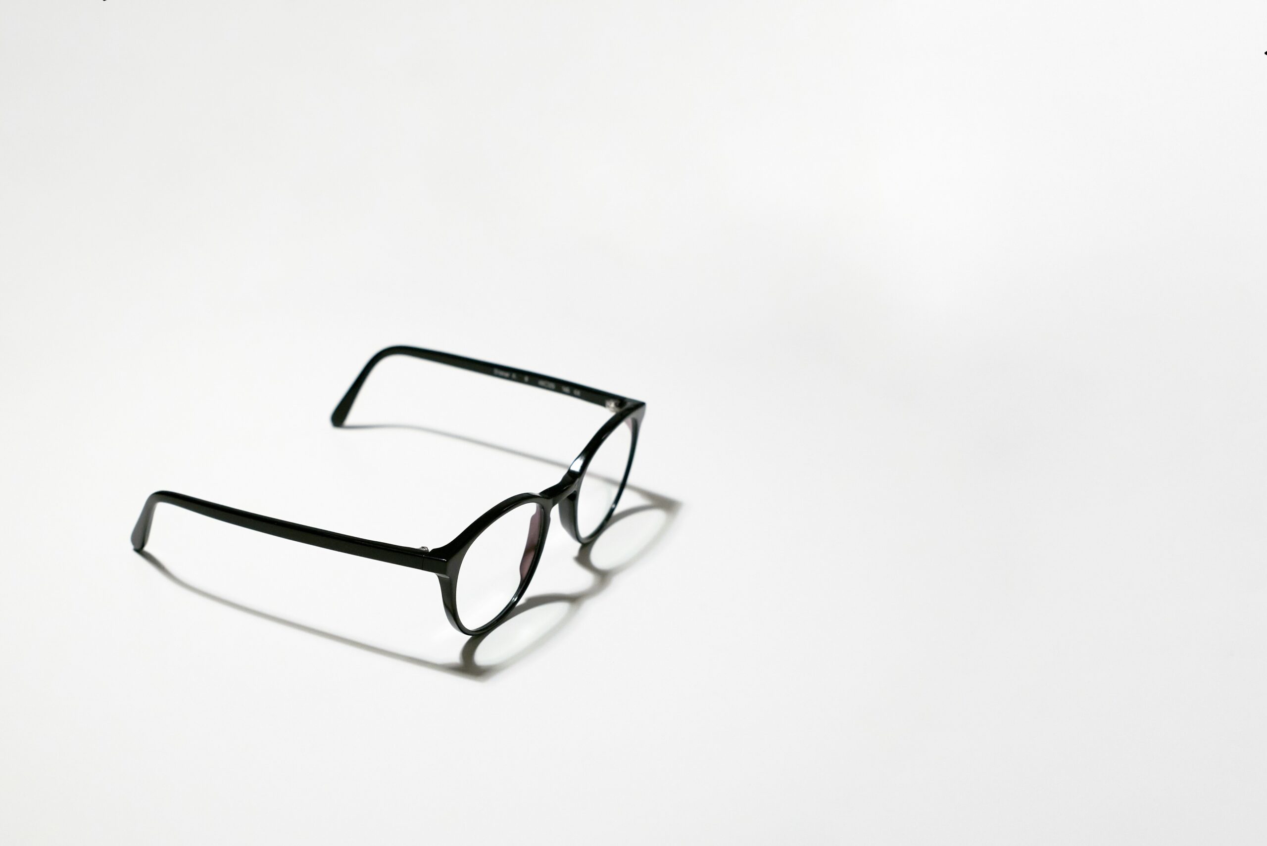 A pair of black-rimmed spectacles on a plain white surface, illustrating how long a glasses prescription is valid in the UK.