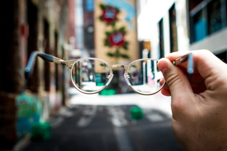 Lentiamo Review UK - Person holding round gold-frame glasses against a colourful street mural