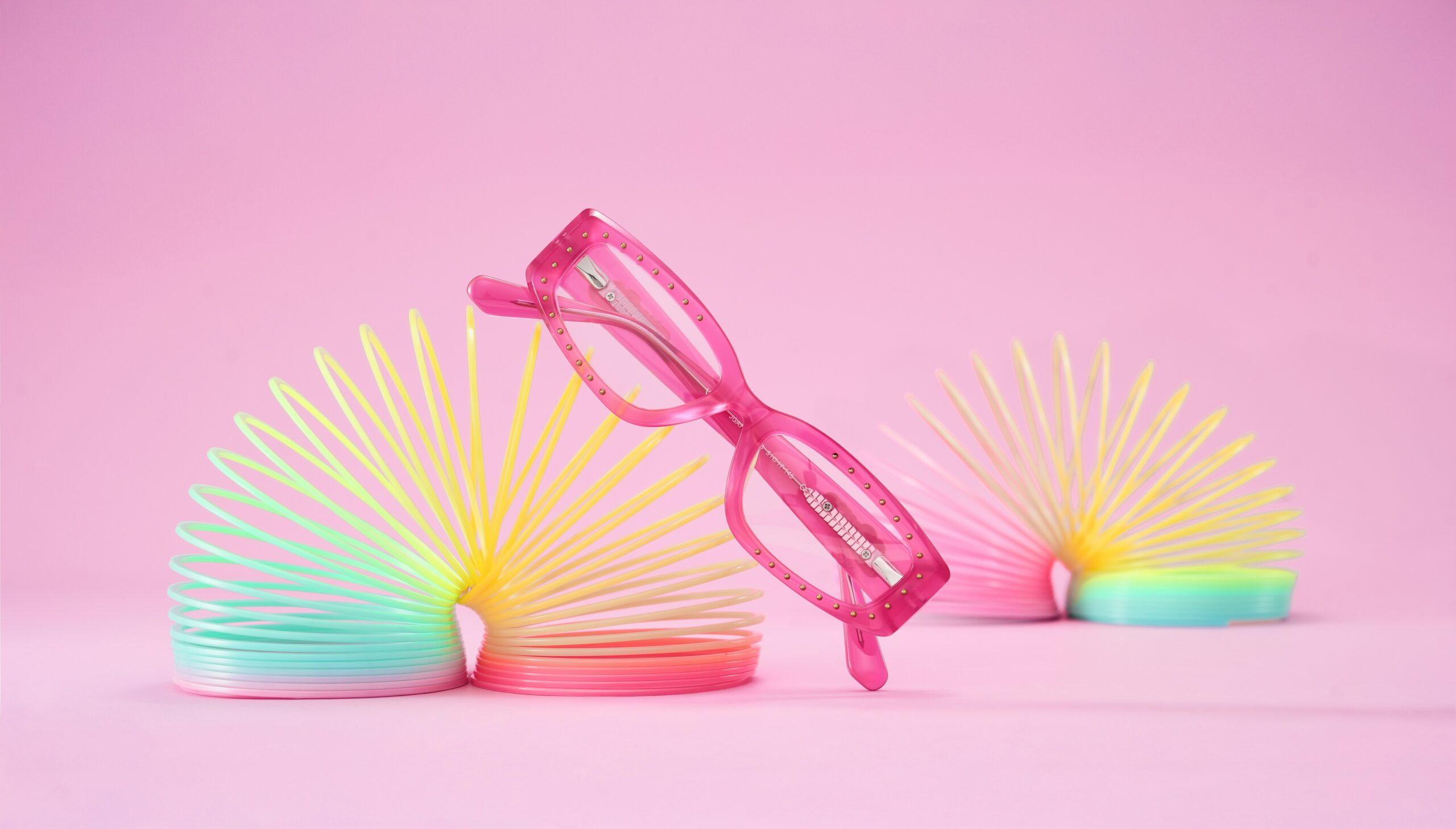 Pink children's glasses resting on colourful slinky toys, illustrating our Stellest lenses parent's guide